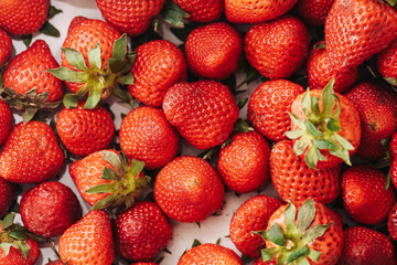 Naklejka premium Ripe strawberries fill the frame with red fruit and green leaves. Juicy seasonal harvest shows natural sweetness. Fresh berry texture creates vibrant food background. Market freshness fills image.