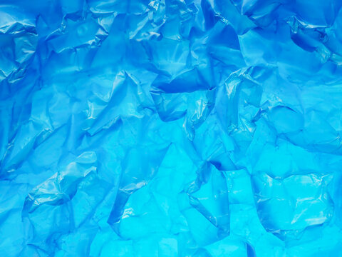 Blue plastic sheet crinkled and wrinkled. Shiny surface catches light in soft glows and reminds of ocean water. Texture suggests use or casual discard. Ideal for abstract or background design
