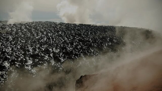 Close-up of solidified lava in circular volcanic crater and columns of steam rising into sky from cracks. Slow motion. Concept of power of wild nature