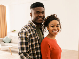 Obraz premium A man and a woman stand together in a living room. They are smiling and looking at the camera. The room has furniture and natural light coming from the windows.