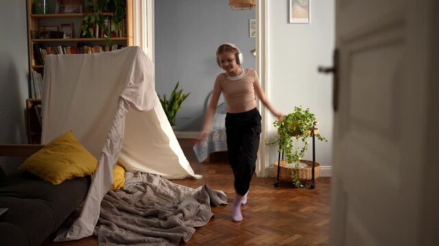 Young girl shows energetic dance moves indoor. An enthusiastic young girl exhibits lively dance steps next to tent within her cozy living space .
