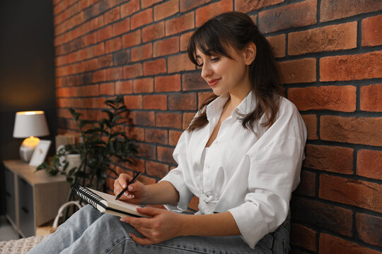Beautiful woman drawing in sketchbook near brick wall