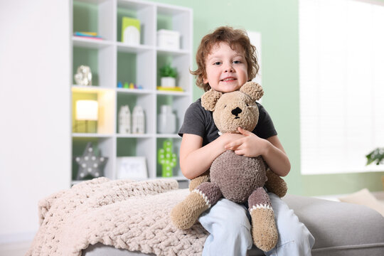 Smiling little boy hugging plush toy bear on pouf at home. Space for text