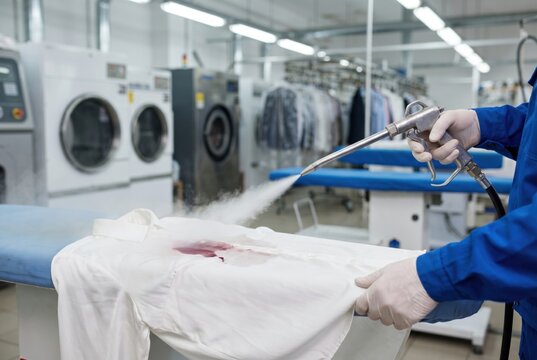 Dry cleaner worker hands wearing gloves using a high pressure steam gun to remove a red stain from a white shirt