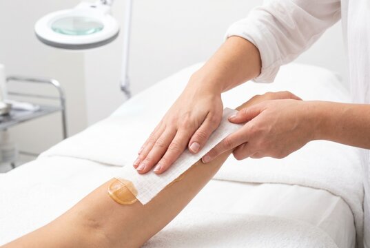 Beautician hands using a white cloth strip to remove sugaring wax from a female client leg in a spa