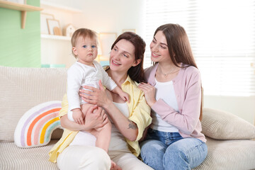 Obraz premium LGBT parents. Happy lesbian couple with their cute baby on sofa at home