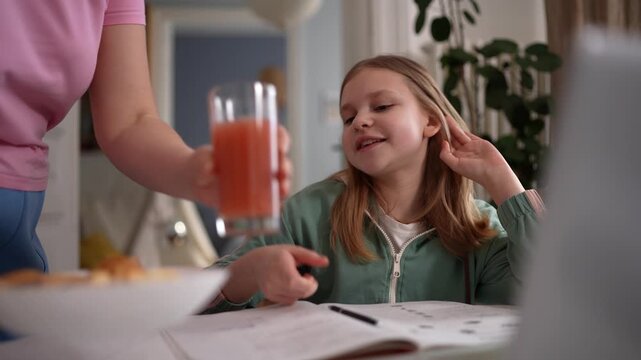 Caucasian girl doing homework at table with laptop notebook and juice, cozy kitchen setting, relaxed concentration, parent offering supportive touch and drink, .