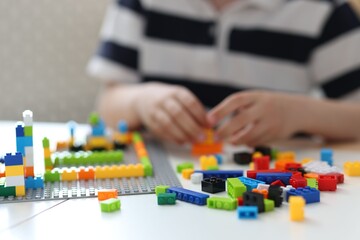 Fototapeta premium Construction toy. Little boy playing with building blocks at table indoors, closeup