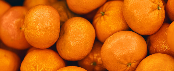 Several oranges are piled high in a grocery store. The bright color of the fruit stands out as shoppers walk by. The setting is lively and the produce section has a fresh feel. © Prostock-studio