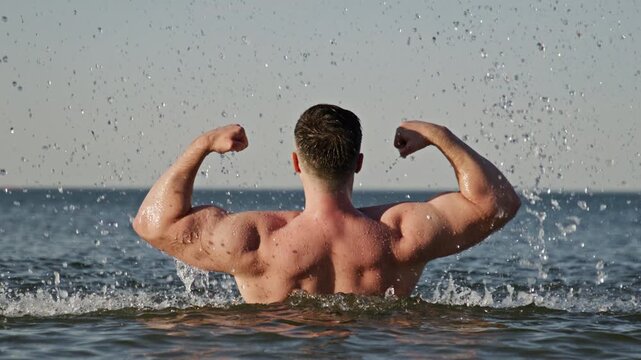 Fitness back shows powerful muscles. Fitness pose looks strong outdoors. Beach fitness concept shows motivation. Wet fitness body shows endurance.