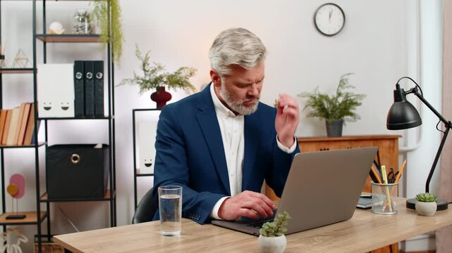 Middle-aged businessman at home office feels fatigue massages temples swallowing headache pill washing with water. Freelancer guy at table prepares to quickly resume tasks relieved pain easing focus.
