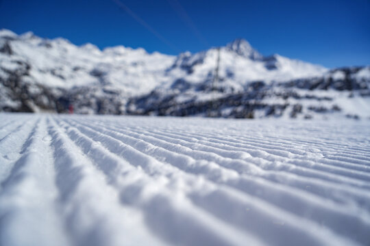 groomed snow corduroy on a ski slope with majestic snow-capped mountains under a clear blue sky in La Thuile, Valle d'Aosta, Italy.