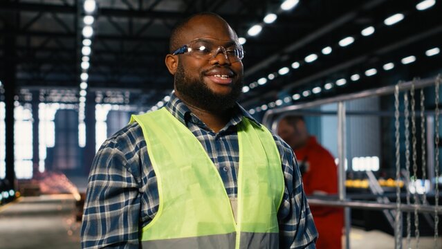 Black technician in a manufacturing facility oversees metal fabrication tools, showing engineering commitment, industrial environment activity and operation on the factory floor.