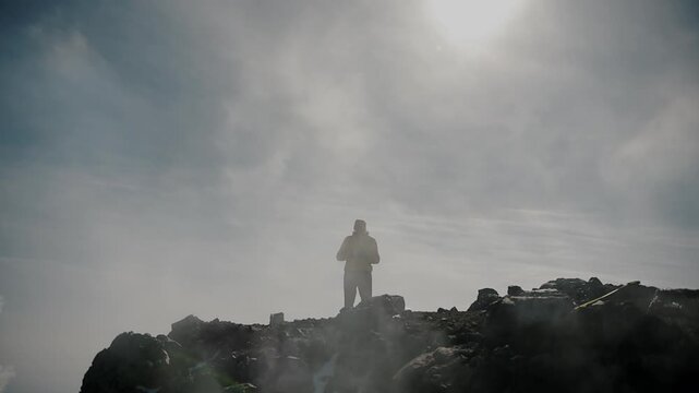 Man stands on edge crater with solidified lava watching as clouds of steam and smoke billow from cracks. Travel and tourism concept