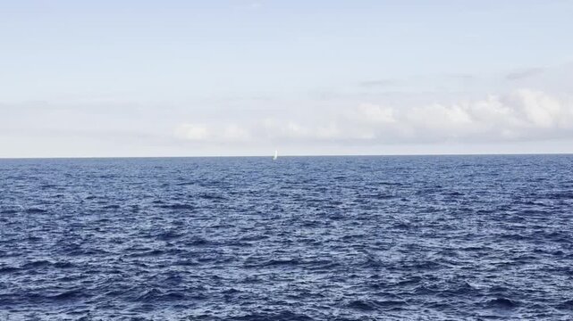 Small sailboat moving slowly along horizon over rippling sea. Loopable ocean footage, smooth repeating waves, peaceful and meditative seascape, minimalist travel vibe.