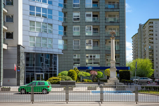 
WARSAW, MAZOWIECKIE, POLAND - MAY 01 2026: A vibrant street view featuring a green compact car parked near a historic column and a modern PZU office.
