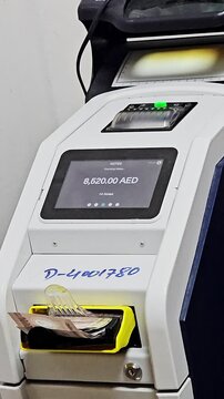 Dubai, Uae - 5th May 2026 :Automated cash deposit machine in Dubai processing  UAE bank notes. Digital screen displays balance while paper currency sits in the yellow feeder tray.