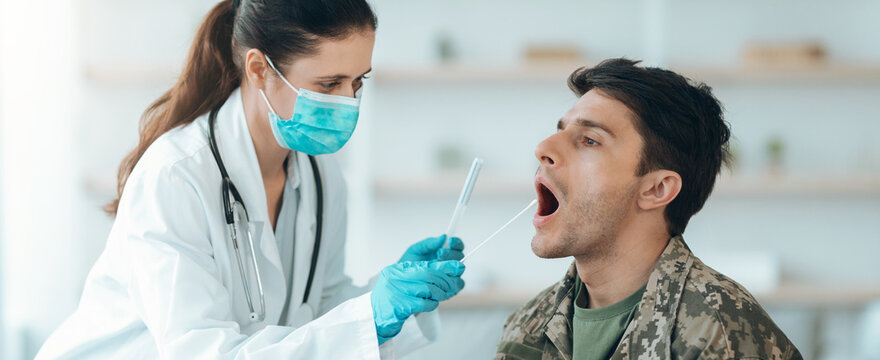 A medical staff member examines a patient in a clinic. The staff is wearing gloves and a mask while using a swab to test the patient's throat. The patient is seated in a chair.