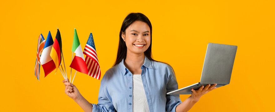 A young woman stands smiling while holding various country flags in one hand and a laptop in the other. The bright yellow background enhances the vivid colors of the flags and her expression.