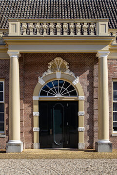 View of the ornate entrance of Castle Groeneveld featuring classic columns, a decorative arched doorway, and red brick walls Baarn, Utrecht, Netherlands.