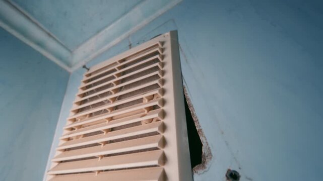 Dirty Ventilation Grille Partially Removed from Blue Wall | Dusty Air Vent with Cobwebs and Damaged Frame | Indoor HVAC Maintenance and Air Quality Concept Close-Up