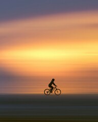 Obraz premium A lone cyclist silhouetted against a bright sunset, panning shot, horizontal motion blur, conceptual image of moving forward