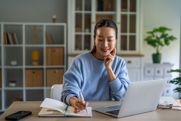 Fototapeta premium Young asian woman working from home office writing notes