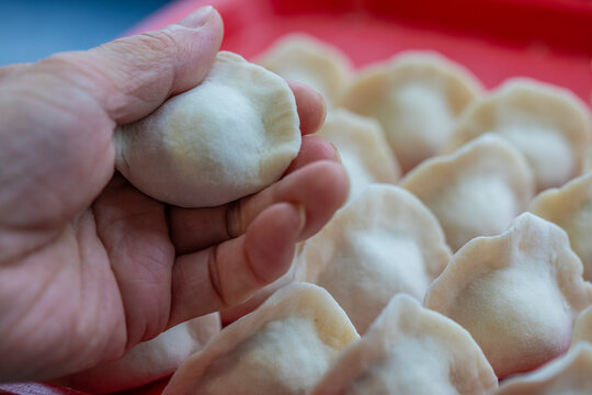 Hand holds fresh made dumpling with more in background