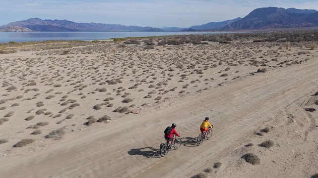 Mature man and woman enjoy biking along sandy trails near La Gringa with views of Bahia De Los Angeles and the Sea of Cortez.
