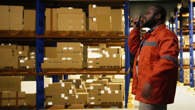 Portable walkie-talkie radio, in distribution hub, black staff member, coordinating shipment details for parcel tracking and cargo handling with two-way transmitter in industrial depot.