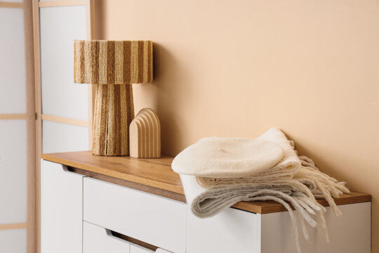 Warm scarves with beret and lamp on commode near beige wall