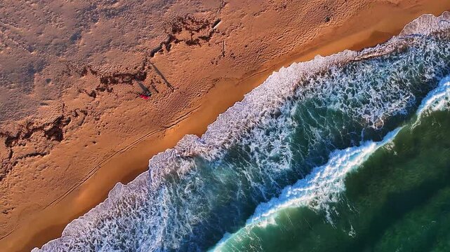 Aerial view of turquoise waves crashing on the sandy beach with white foam and textured sand in Costa Paradiso, Sardegna, Italy.