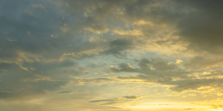 Panoramic sunset sky background with soft golden clouds and vibrant yellow glow at the horizon under a twilight sky