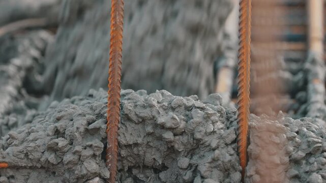 Fresh concrete mix filling formwork around vertical rebar close up