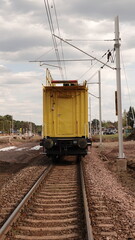 Żółty wagon techniczny stoi na torowisku podczas prac modernizacyjnych linii kolejowej. Nad szynami widoczna jest sieć trakcyjna, a w oddali trwają intensywne roboty przy infrastrukturze kolejowej © tomo81