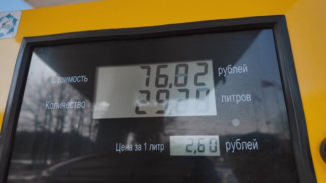 Yellow gas pump digital display showing rising cost in rubles and liters during vehicle refueling, closeup of fuel counter reflecting increasing gasoline price and consumption