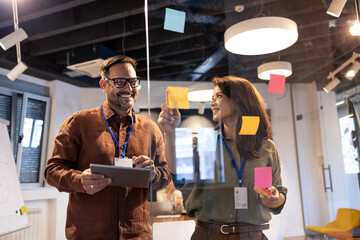 Business professionals collaborating on a project, brainstorming ideas with sticky notes on a glass board in an office © littlewolf1989