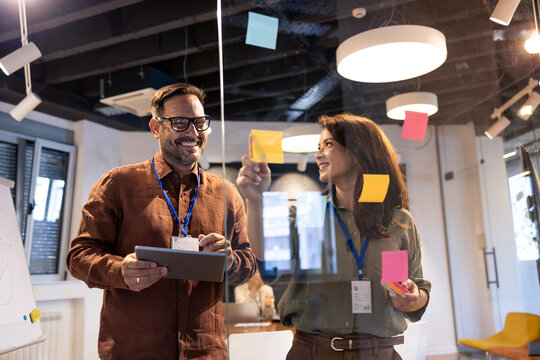 Business professionals collaborating on a project, brainstorming ideas with sticky notes on a glass board in an office