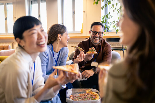 Colleagues enjoying pizza lunch, laughing and bonding during an informal team building event at the office