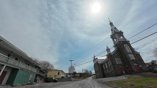 Cinematic dashcam footage of a narrow street leading to St-Octave-de-M&eacute;tis Church, a historic landmark with a tall steeple in rural Quebec, Canada.