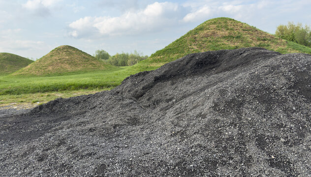 Black coal slag pile with grassy hills in industrial landscape