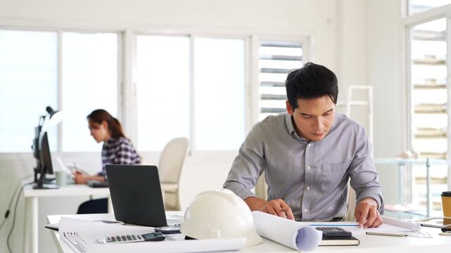 Young asian civil engineer studying a blueprint floor plan and  working with documents, drawings and building models.
