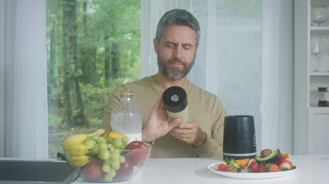 Man preparing healthy smoothie at home. Bearded man using blender in kitchen. Healthy breakfast smoothie preparation. Man making fresh fruit drink. Homemade smoothie for healthy lifestyle.