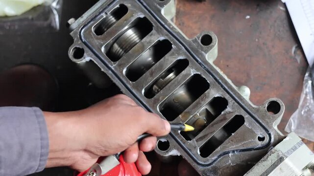 ​A professional mechanic uses a red oil can to apply lubricant to the metal valves and internal parts of an engine component during a repair process in an automotive workshop.