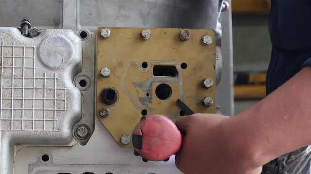 ​A technician uses a red power impact tool to tighten bolts on a yellow metal housing plate during a heavy machinery engine overhaul in a professional workshop.