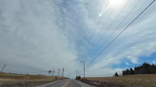 4K dashcam footage of a winding rural road passing electricity pylons in yellow agricultural fields, showcasing the contrast between natural countryside and industrial power infrastructure.