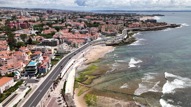 Aerial view of the rocky coastline and sandy beaches of Parede with residential buildings and a coastal road under a cloudy sky Parede, Lisbon, Portugal.