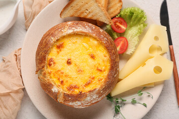 Obraz premium Cheese soup in bread bowl with lettuce, toasts, micro green and cut tomato on light background