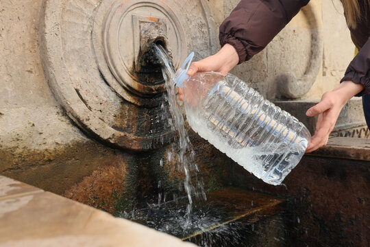 Woman filling plastic bottle from public water source outdoors