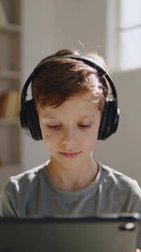Young boy wearing black headphones using tablet in bright room, eye level, interior, copy space